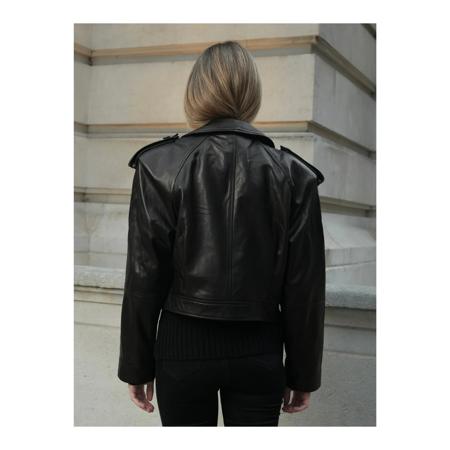Person wearing a black leather jacket standing on a staircase.